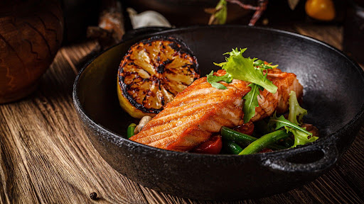 Seared salmon fillet showing quality texture, served with charred lemon and vegetables.